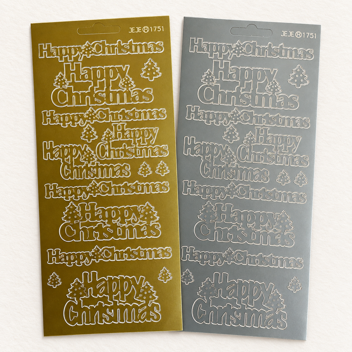 Two Christmas-themed sticker sheets with 'Happy Christmas' text and tree motifs, shown side by side on a light background. One sheet is metallic gold and the other is silver.