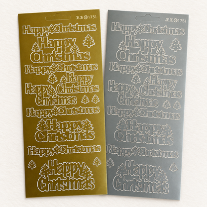 Two Christmas-themed sticker sheets with 'Happy Christmas' text and tree motifs, shown side by side on a light background. One sheet is metallic gold and the other is silver.