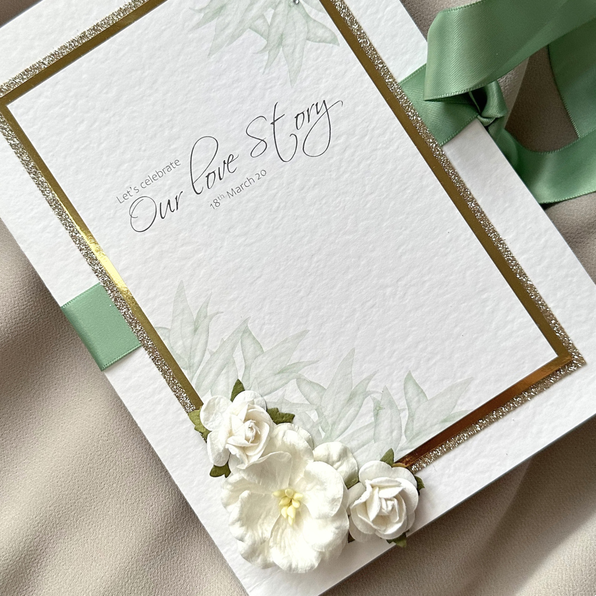 Luxury sage green and gold wedding invitation with layered card, satin ribbon and handmade white paper flowers
