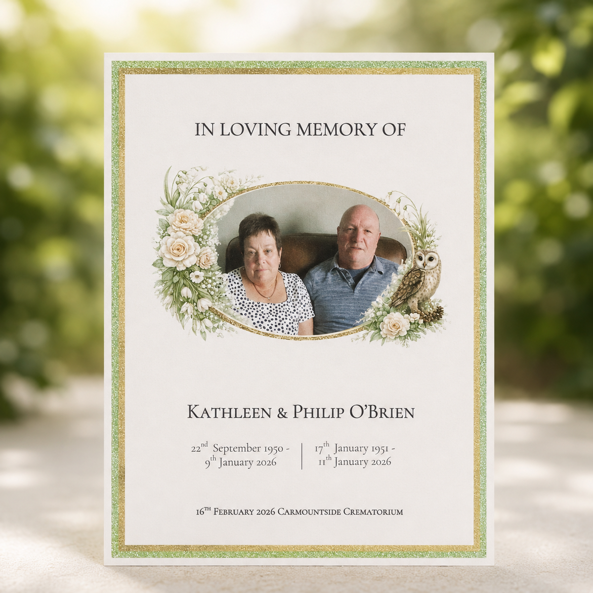A personalized memorial card with a photo of a couple, floral accents, and their names and dates of death and burial, shown standing against a blurred green outdoor background.