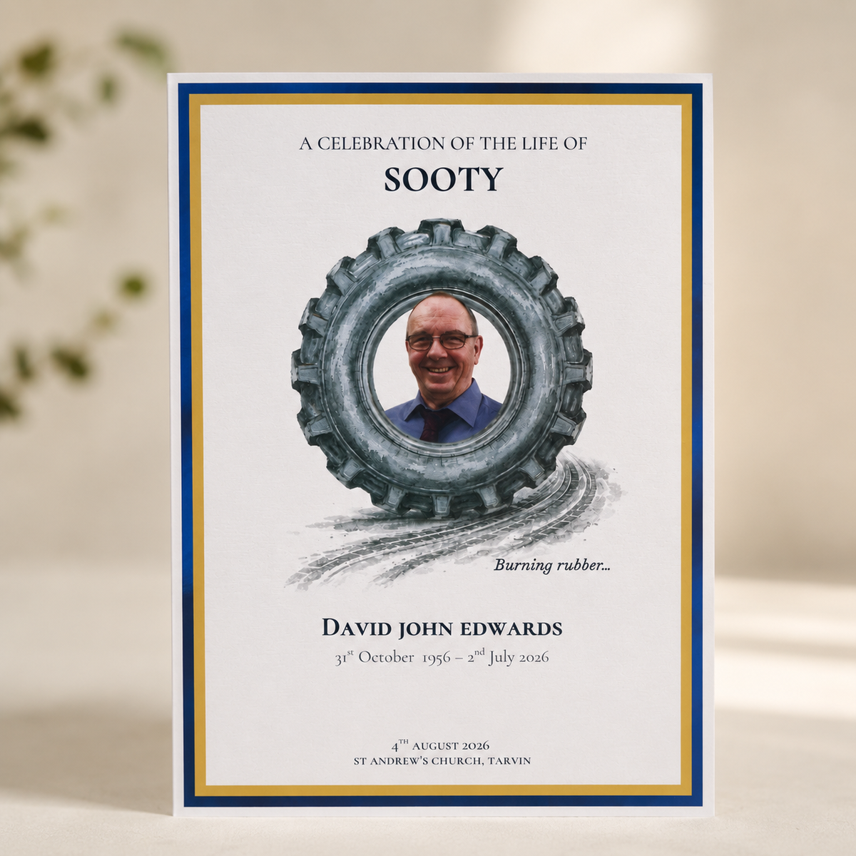 A personalized memorial card for 'Sooty' featuring a photo of a man inside a tyre illustration, with blue and gold borders on a white card, set against a softly blurred background.