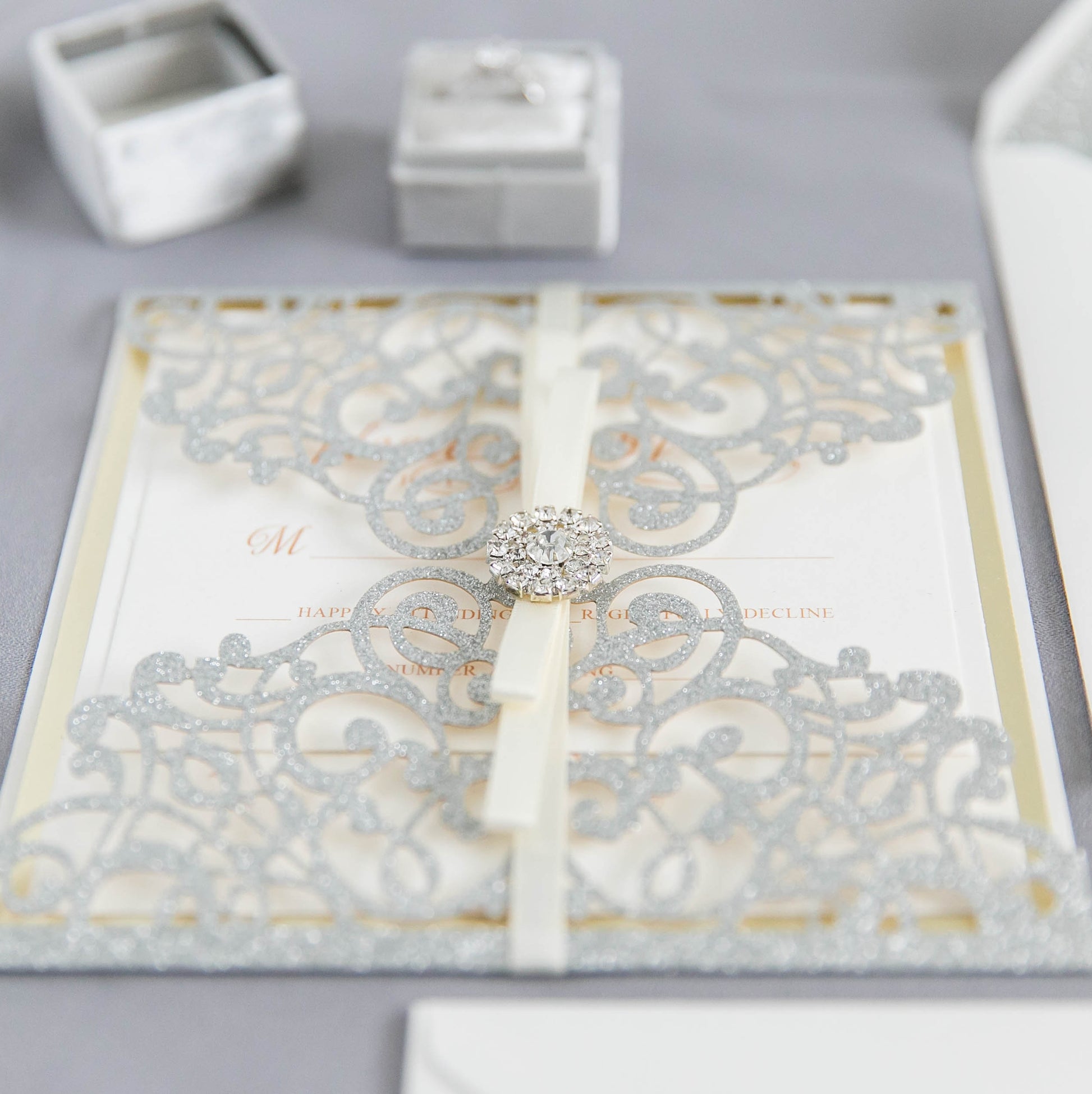 close up of diamante embellishment on silver glitter wedding invitation